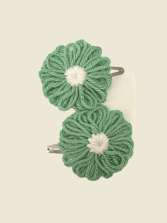Two green yarn flowers snap clips with white centers on a gray surface