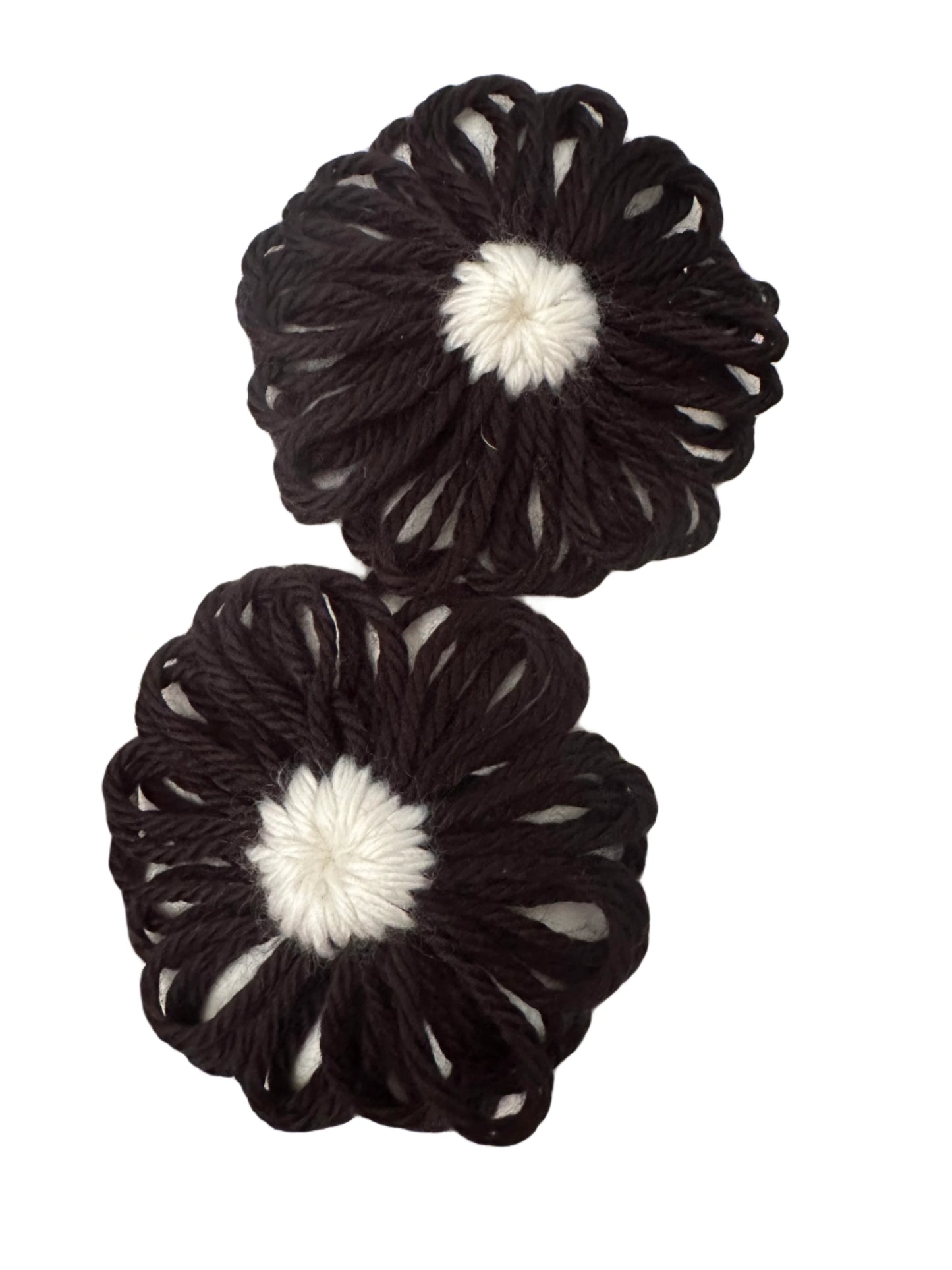 Two black with white centers yarn flowers snap clips with white centers on a gray surface