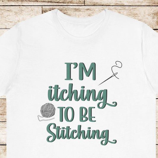 Funny Itching to be Stitching white colored T-Shirt with heather teal lettering, a ball of yarn, and a needle with thread