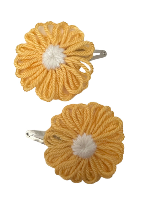 Two yellow yarn flowers snap clips with white centers on a gray surface