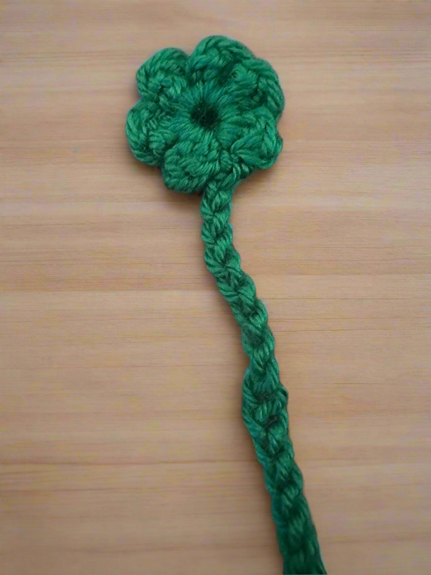 Green crocheted flower bookmark with a stem on a wooden surface
