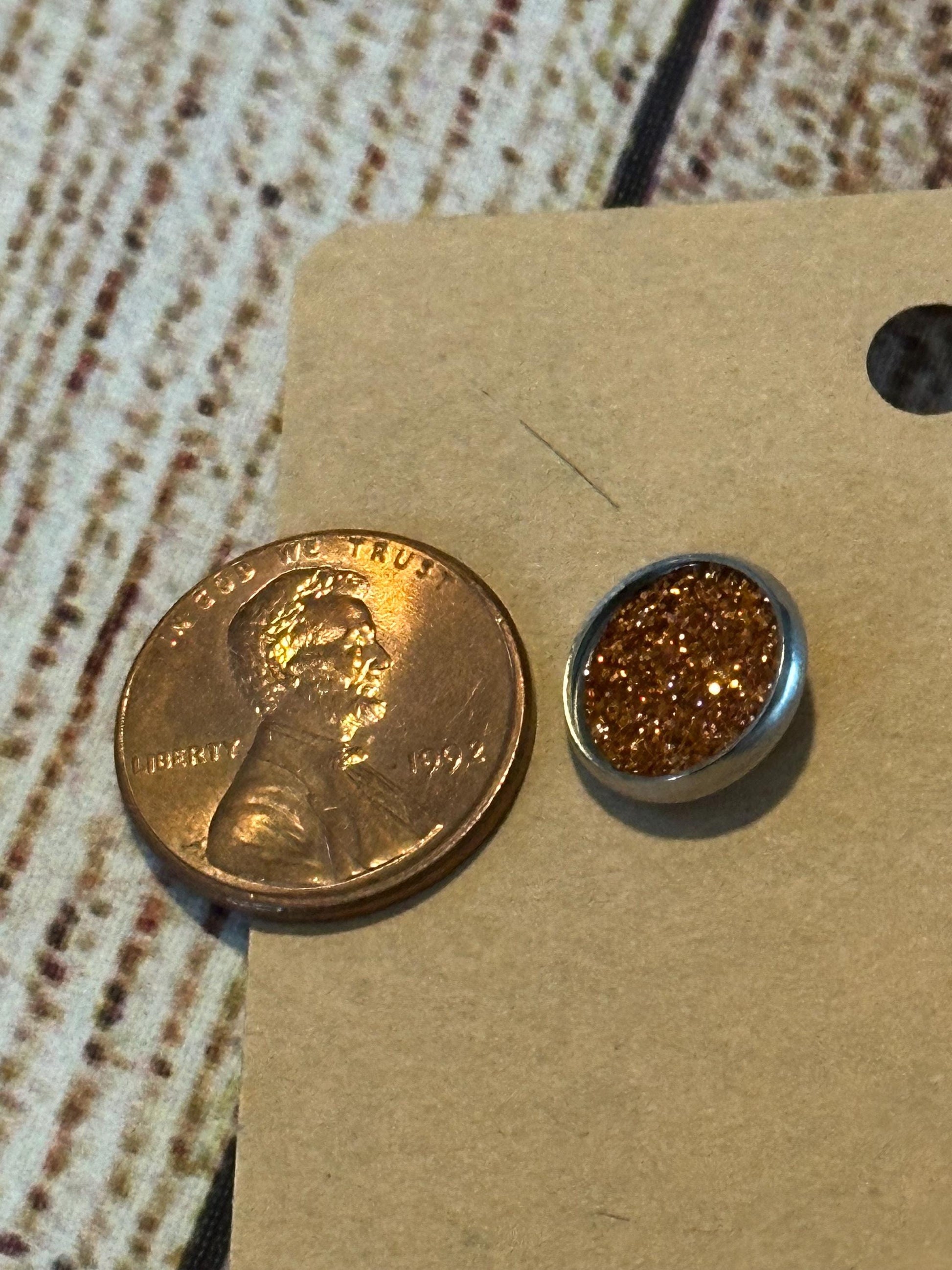 round stud earrings with a glittery orange faux leather center with a penny to show size