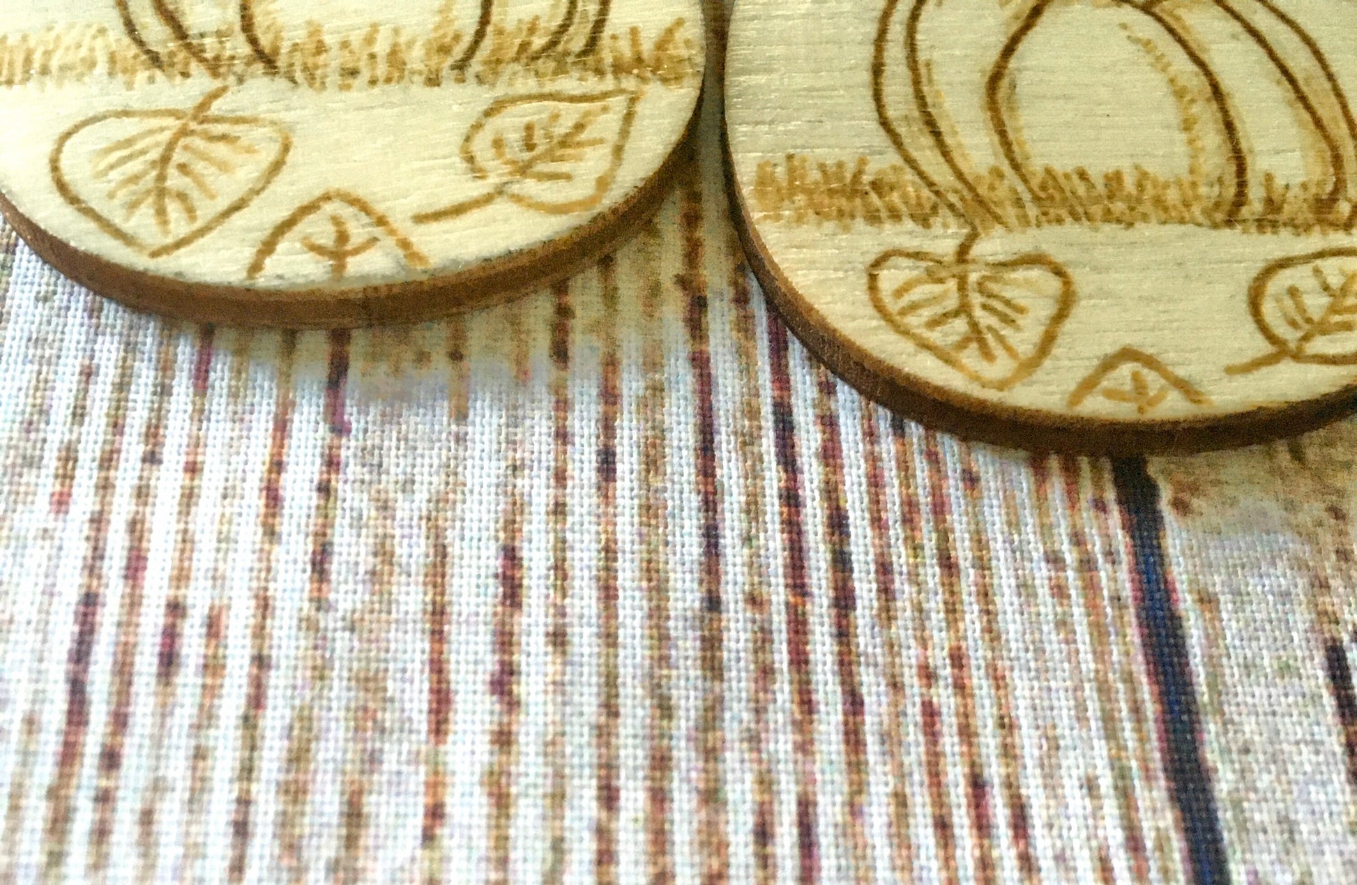 Wood burned earrings with wood burned pumpkin sitting in the grass with leaves on the ground. Earrings are tear drop shaped with fishhooks.