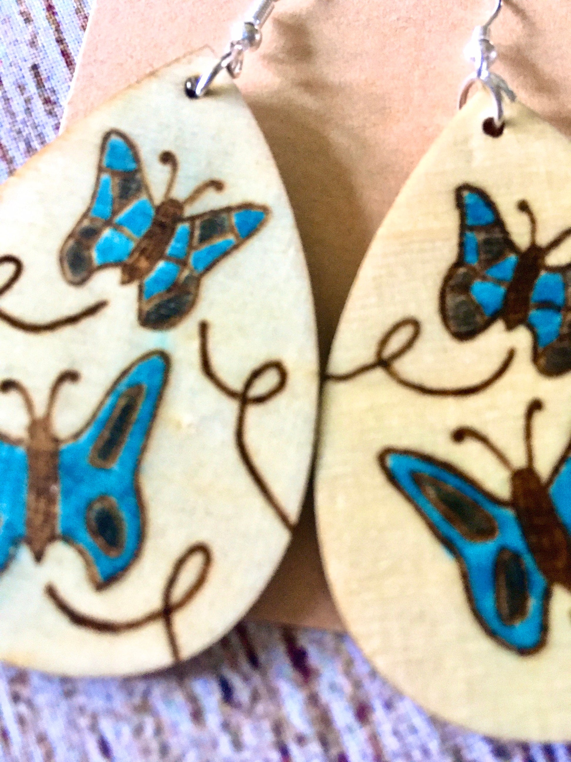 Wood burned earrings wood burned with butterflies colored blue.  Earrings have fishhooks and are teardrop shape.