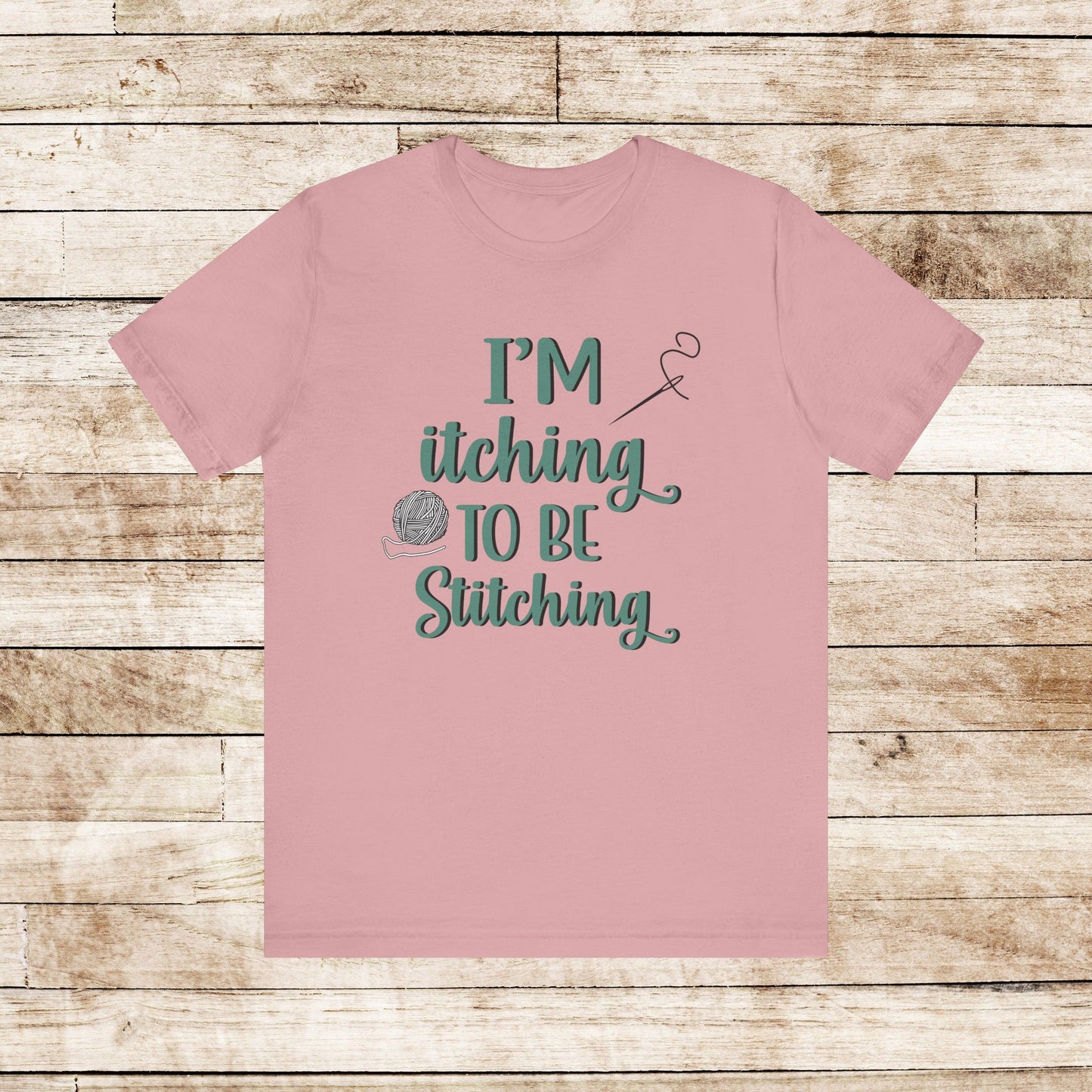 Funny Itching to be Stitching orchid colored T-Shirt with heather teal lettering, a ball of yarn, and a needle with thread