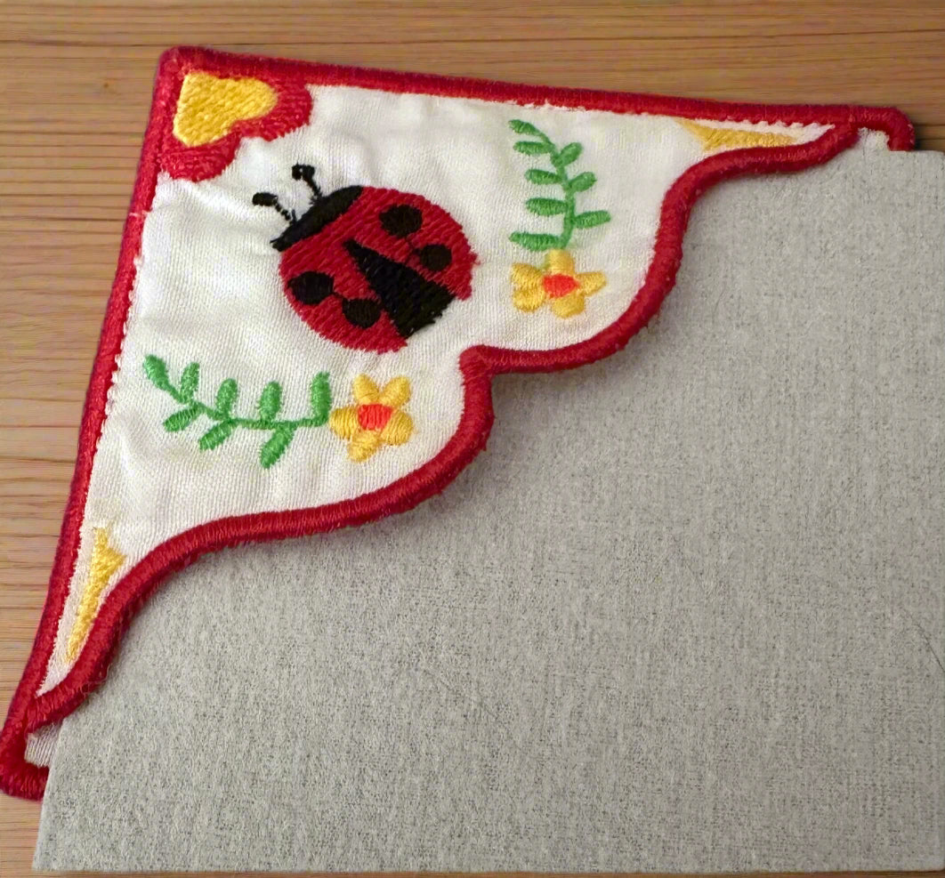 Embroidered corner bookmark with a ladybug design on a wooden background
