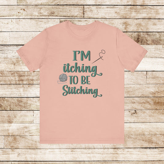 Funny Itching to be Stitching peachcolored T-Shirt with heather teal lettering, a ball of yarn, and a needle with thread