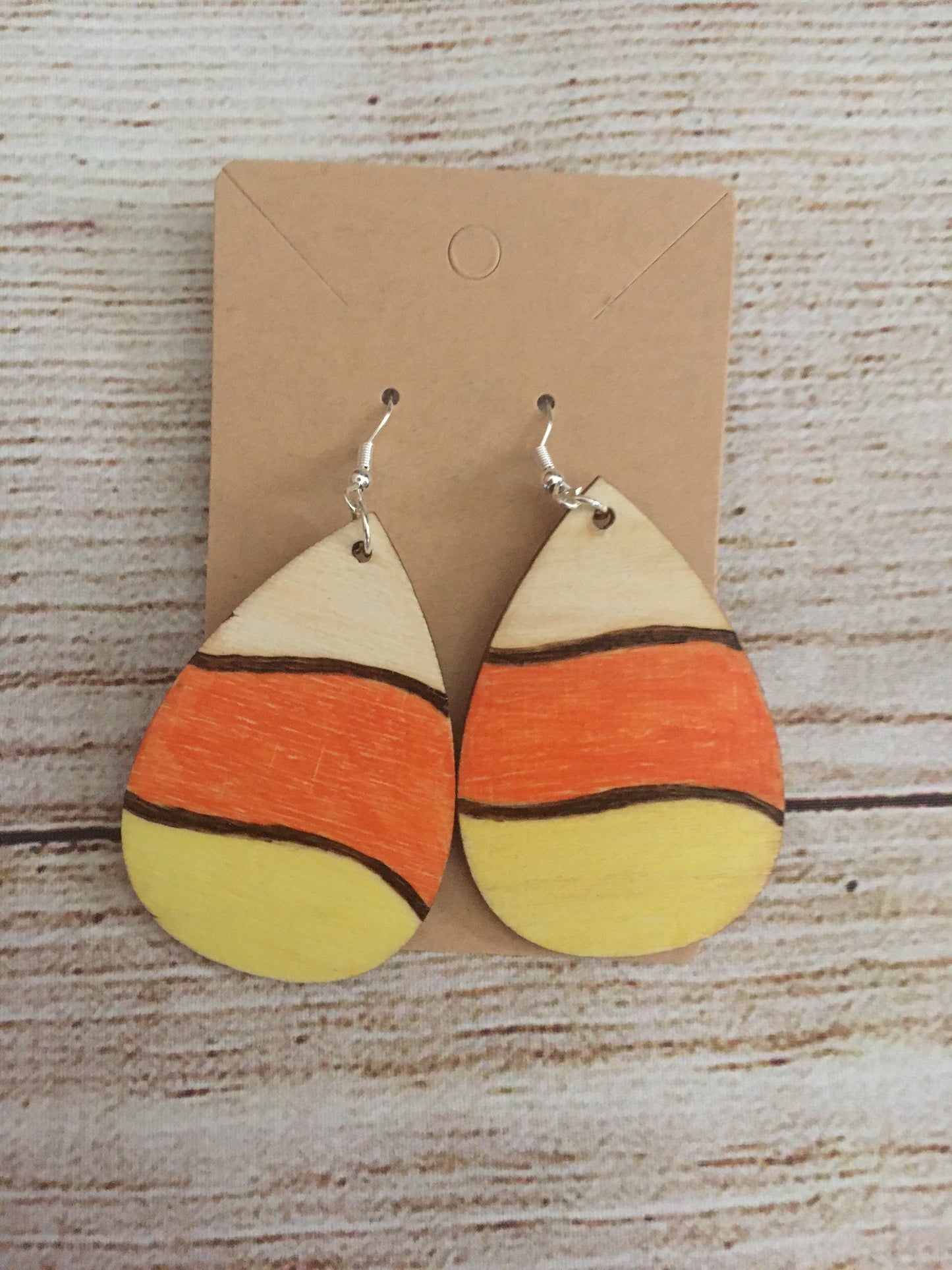 Wood burned earrings wood burned and colored like Halloween candy corn- white, orange, and yellow. Earrings have fishhooks and are teardrop shape.