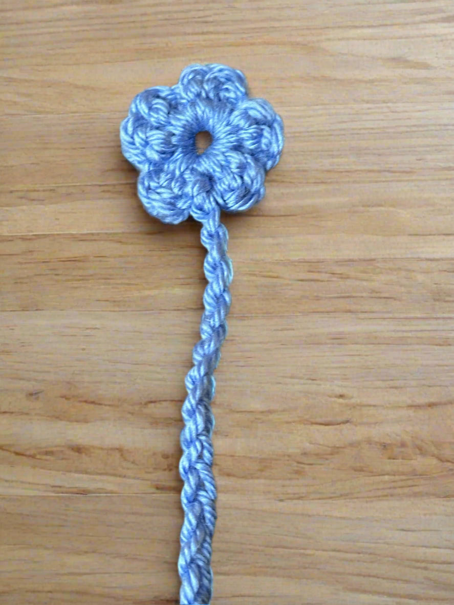 Blue crocheted flower bookmark with a stem on a wooden surface