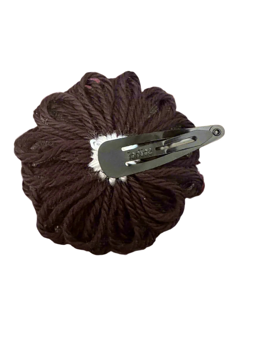 black with white yarn flowers snap clip on a gray surface with a metal clip on a white background