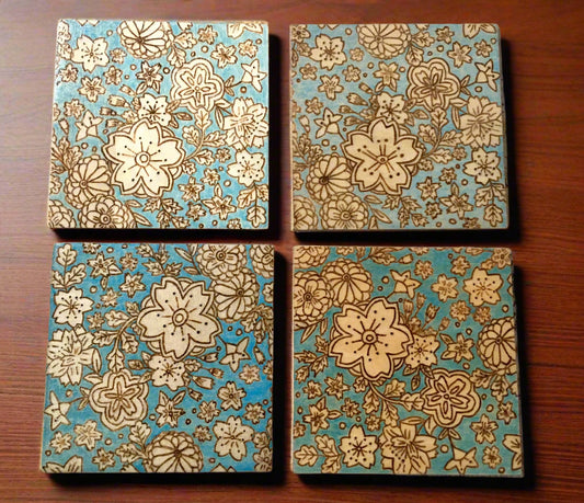 set of 4 wooden coasters.  coasters are wood burned featuring different types of flowers.  The coasters have a blue colored background