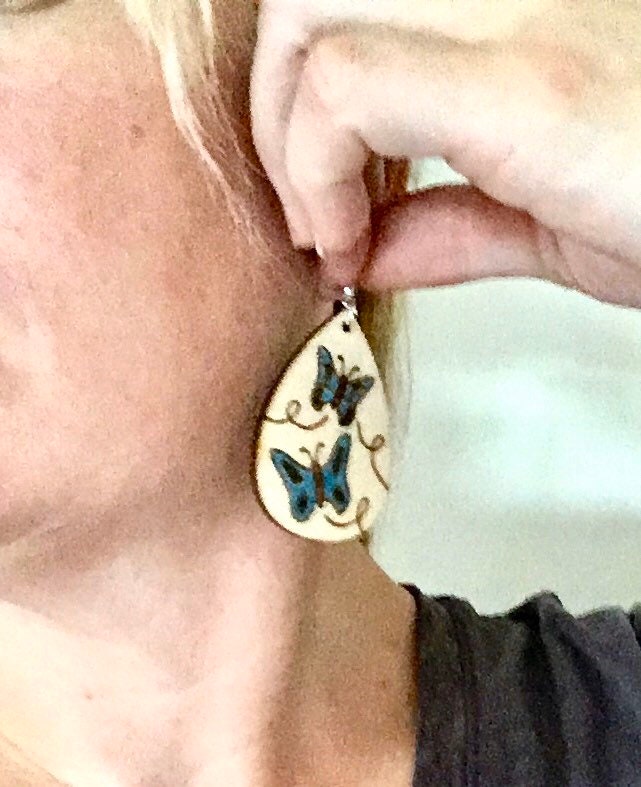 Wood burned earrings wood burned with butterflies colored blue.  Earrings have fishhooks and are teardrop shape.