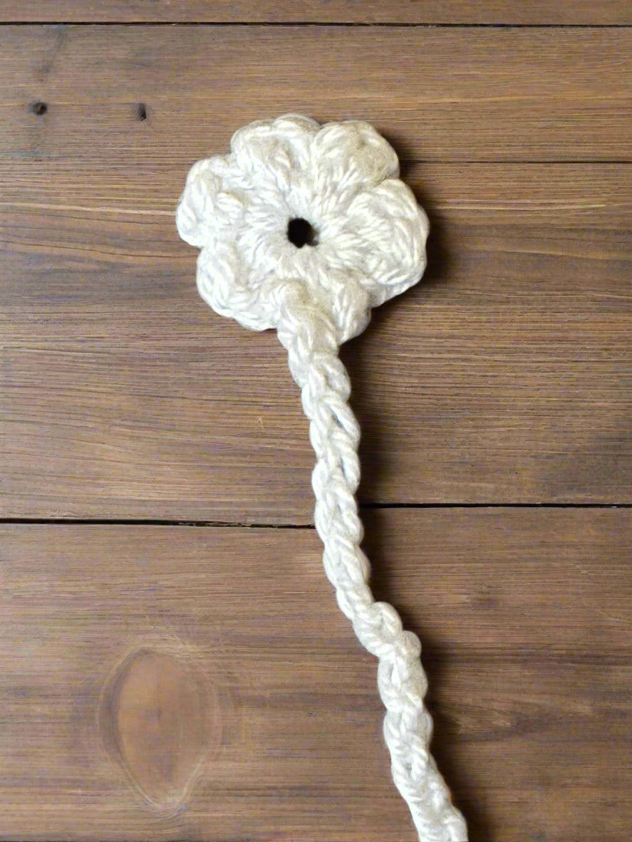 White crocheted flower bookmark with a long stem on a wooden surface