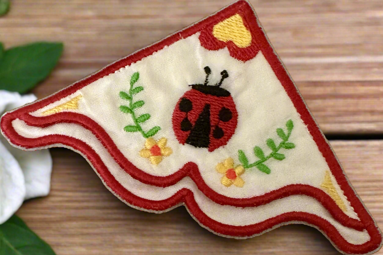 Embroidered corner bookmark with a ladybug design on a wooden surface