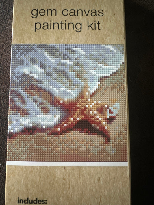 Gem canvas painting kit packaging with a starfish design on the beach at the edge of the water on a brown background