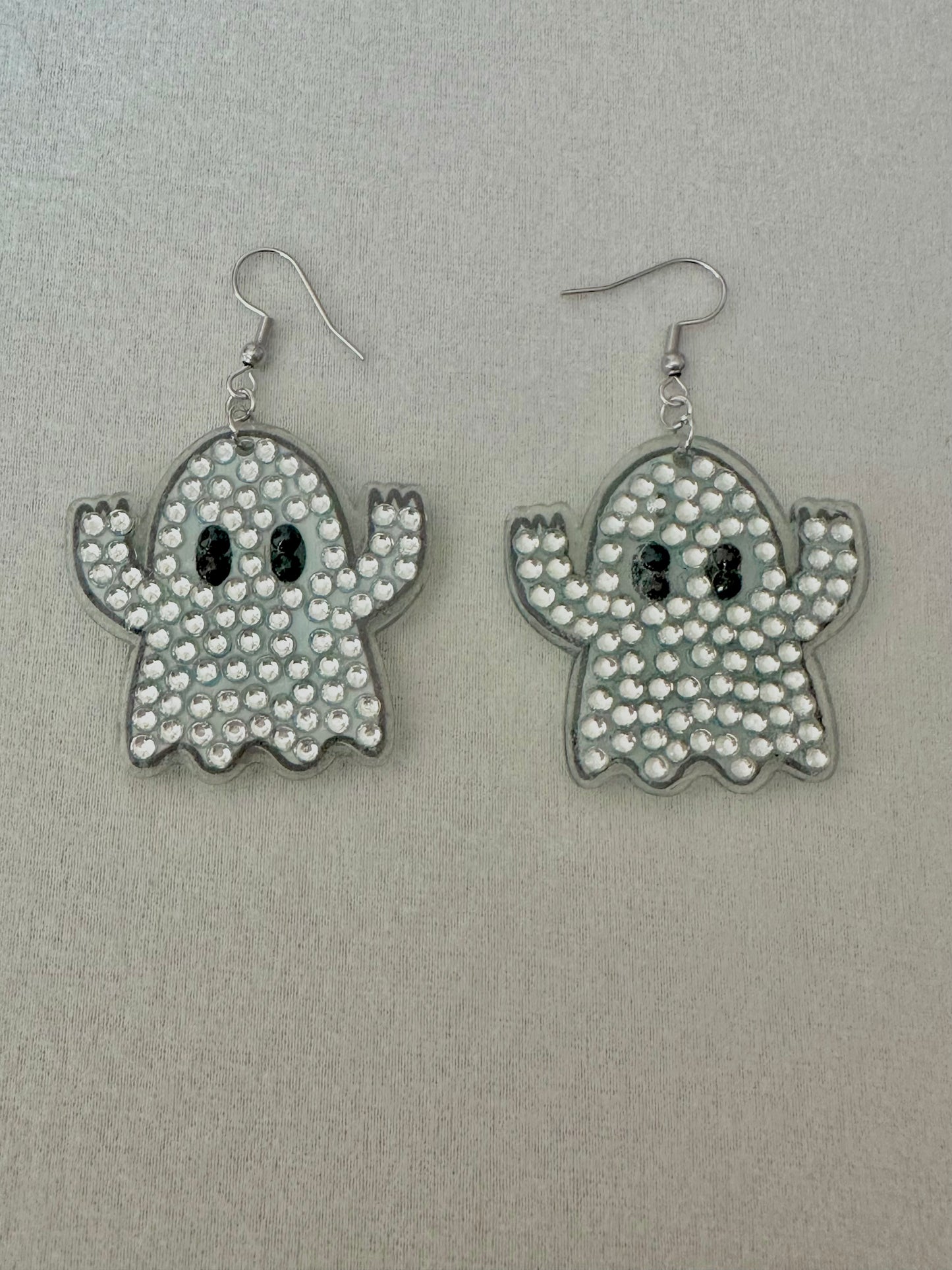 Ghost-shaped earrings with rhinestone detailing on a gray background
