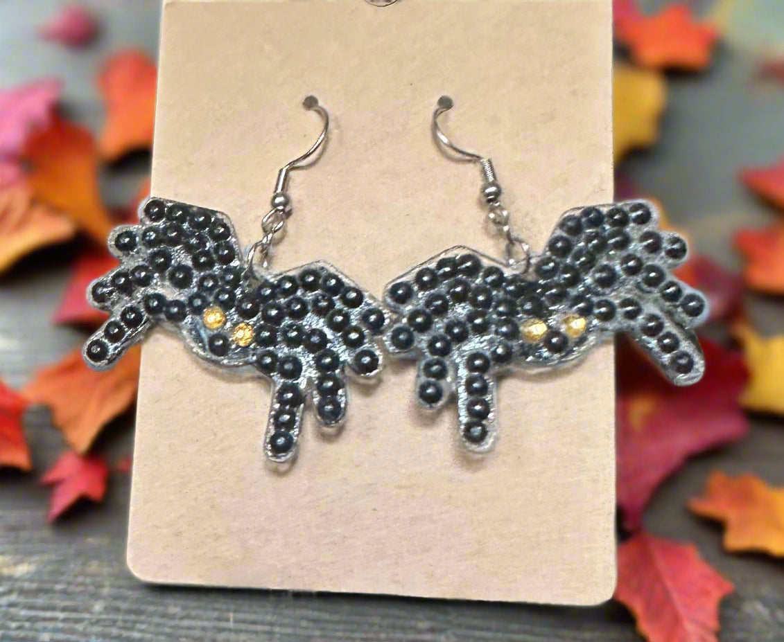 Black beaded spider earrings on a beige card with autumn leaves in the background