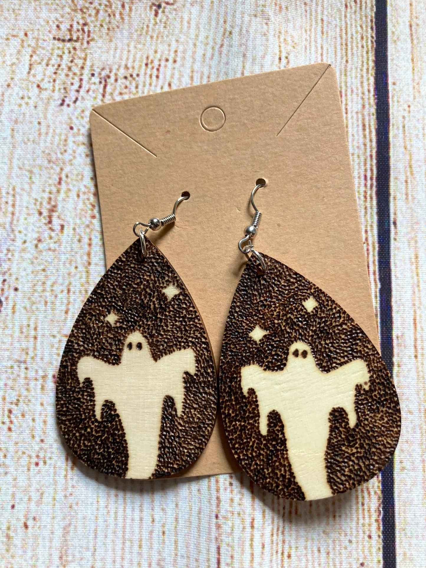 Wood burned earrings wood burned featuring a Halloween ghost on a dark wood burned background Earrings have fishhooks and are teardrop shape.
