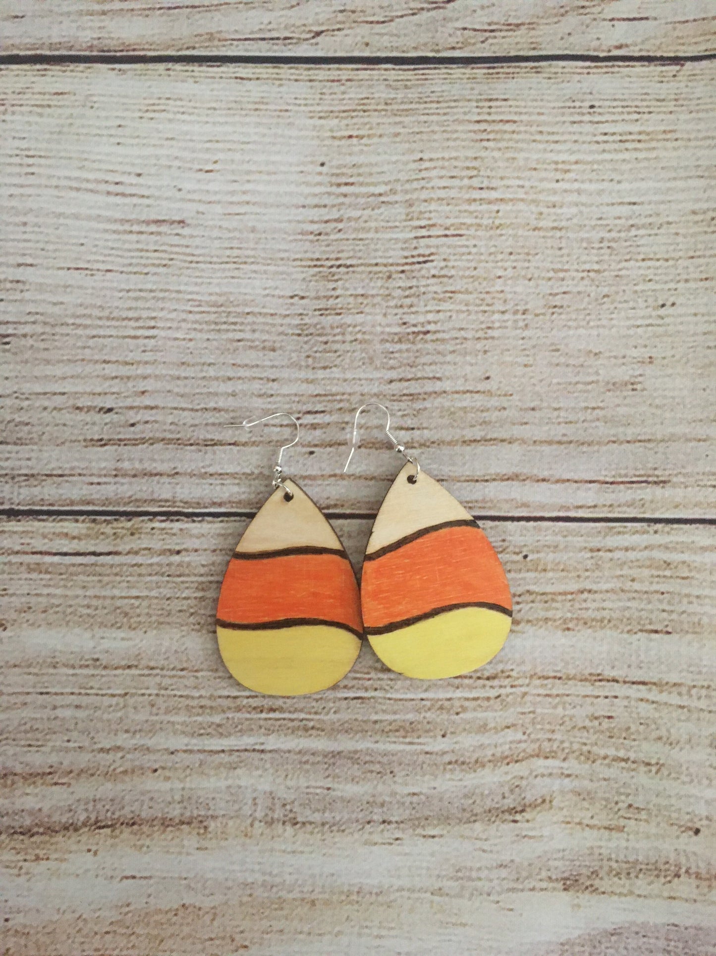 Wood burned earrings wood burned and colored like Halloween candy corn- white, orange, and yellow. Earrings have fishhooks and are teardrop shape.