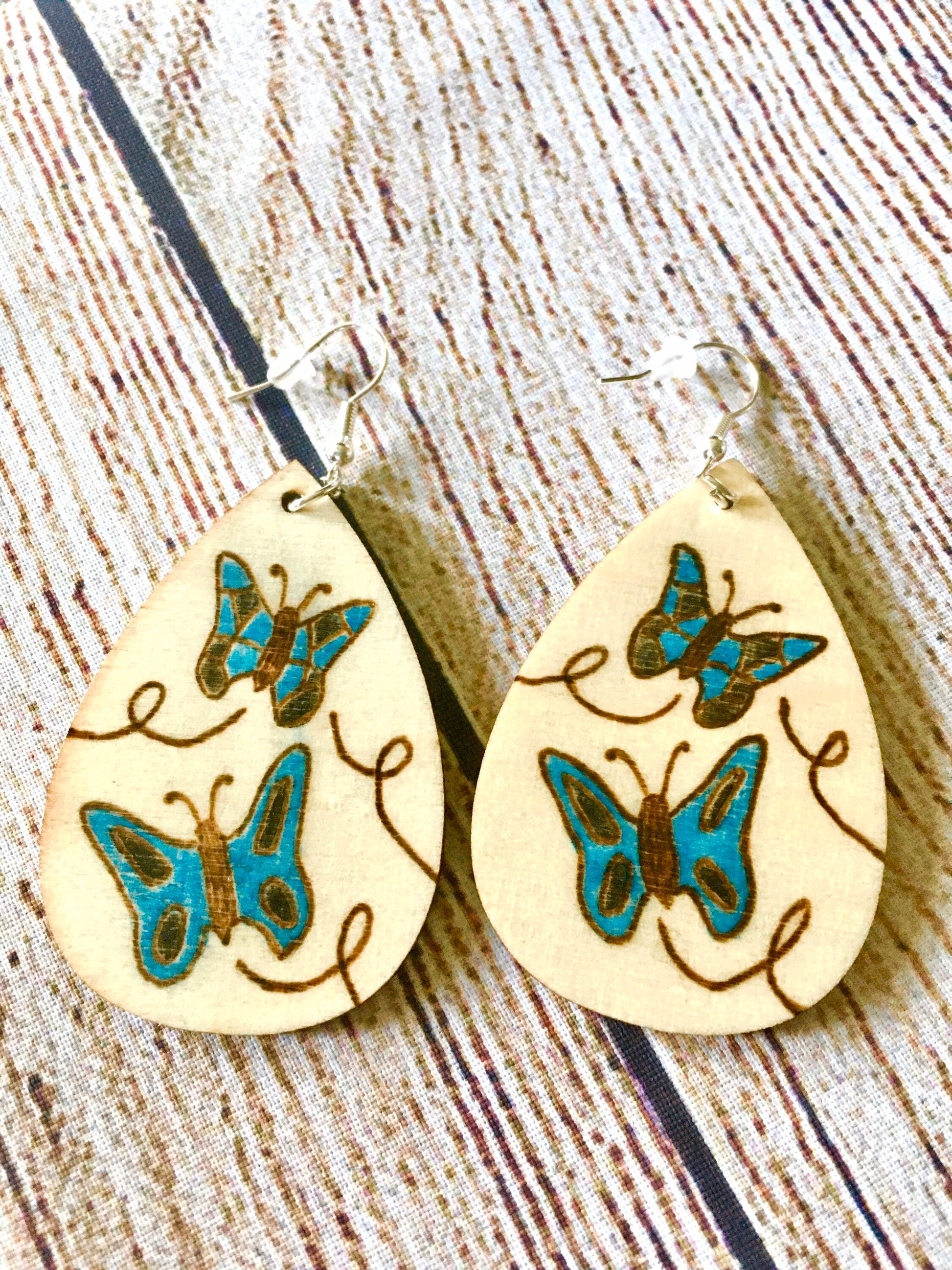 Wood burned earrings wood burned with butterflies colored blue.  Earrings have fishhooks and are teardrop shape.