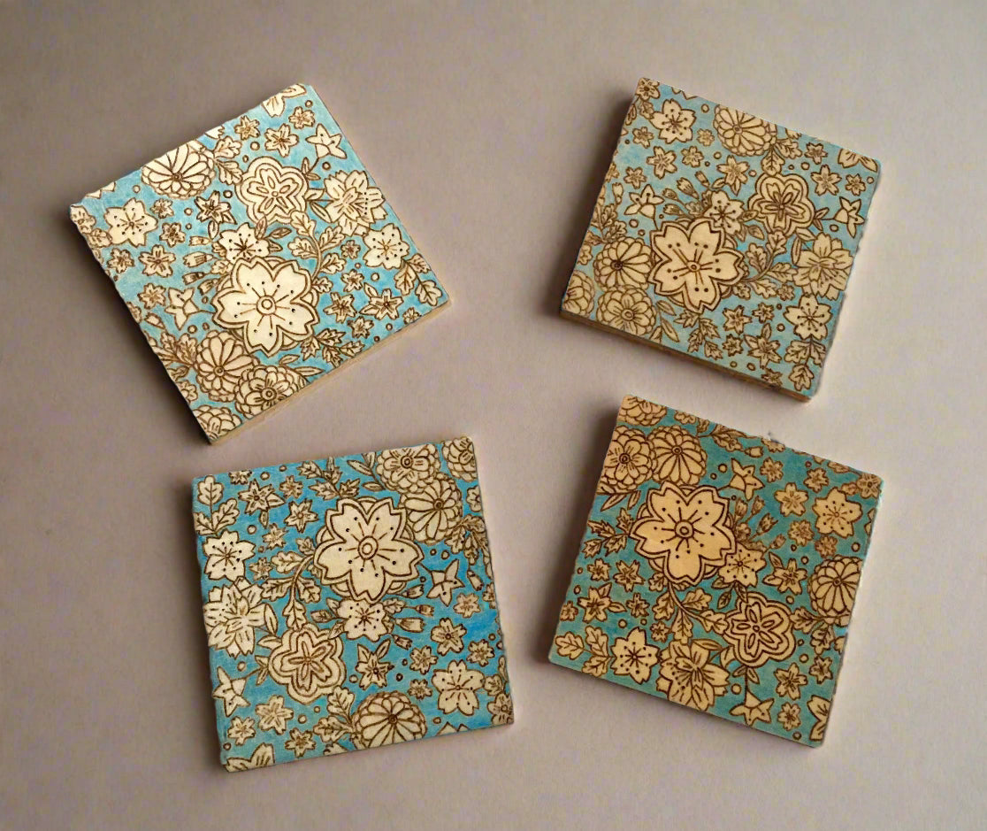set of 4 wooden coasters.  coasters are wood burned featuring different types of flowers.  The coasters have a blue colored background