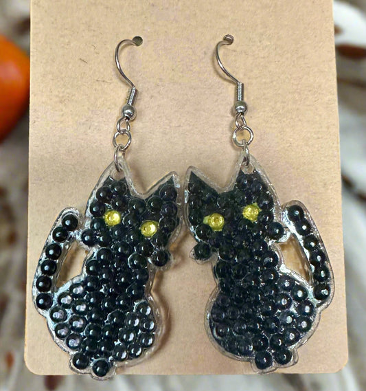 Black cat-shaped earrings with yellow eyes on a cardboard backing