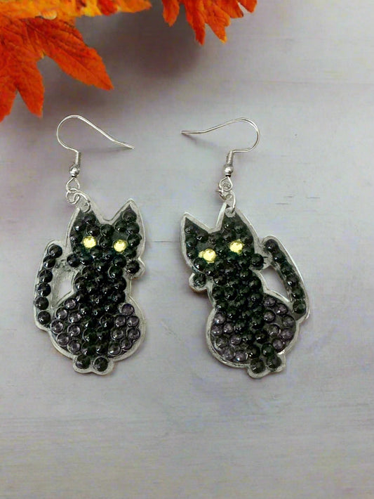 Black cat-shaped earrings with yellow eyes on a light gray background