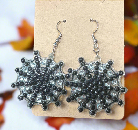 Pair of black and silver cobweb earrings on a cardboard display.