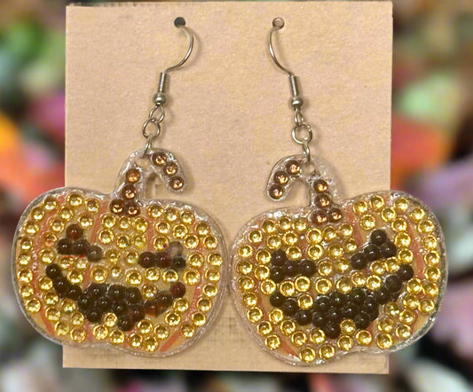 Pumpkin-shaped earrings with gold beads and black details on a beige card.