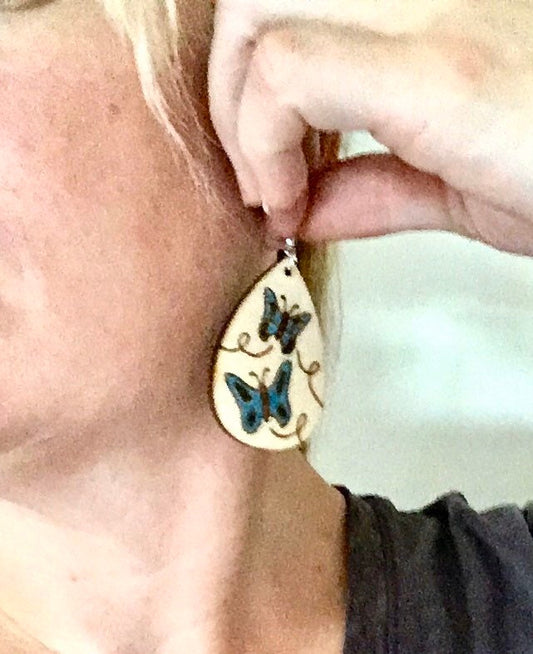 Wood burned earrings wood burned with butterflies colored blue.  Earrings have fishhooks and are teardrop shape.