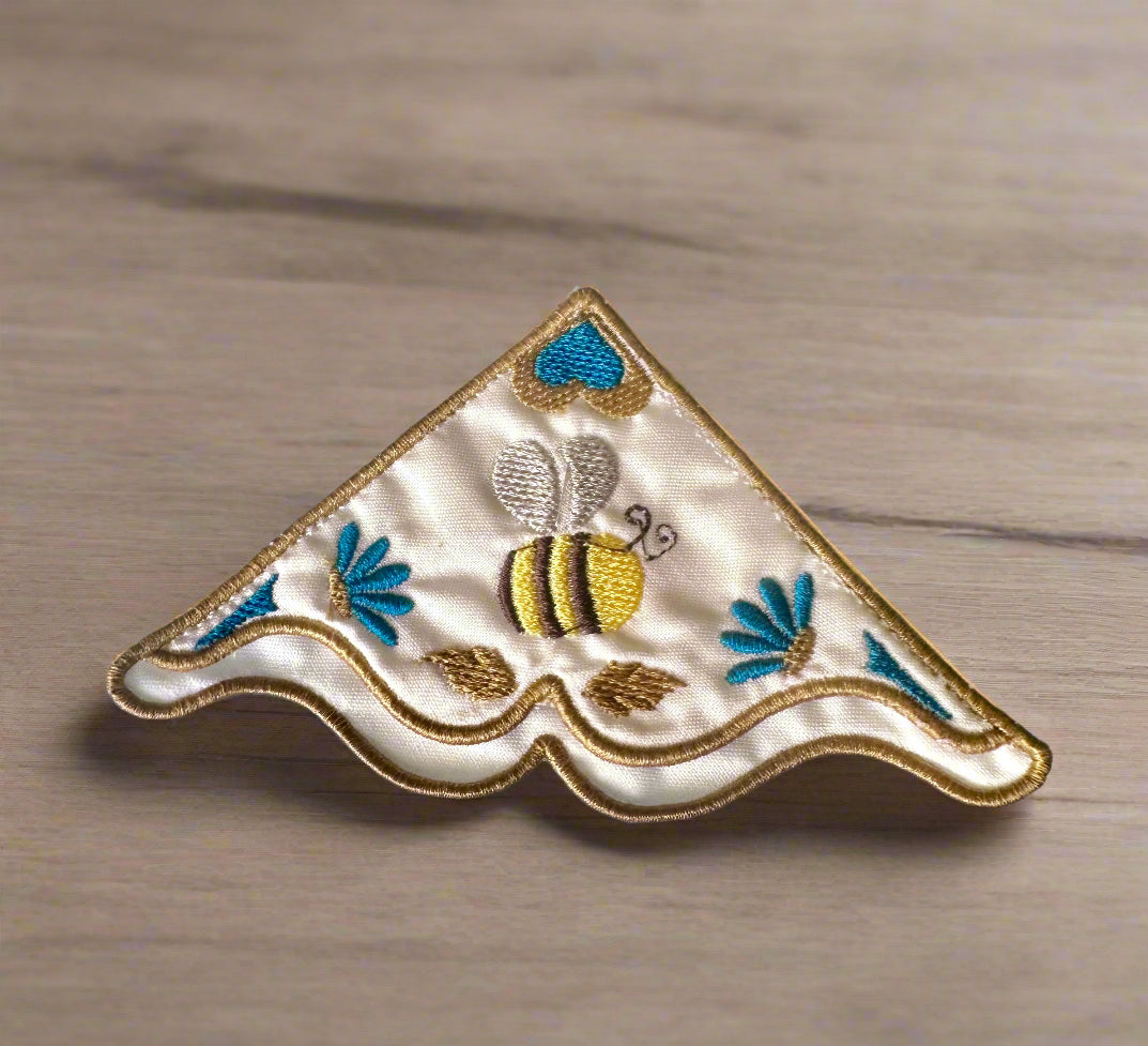 Embroidered corner bookmark with a bee design on a wooden surface