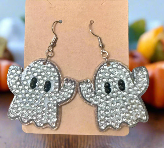 Ghost-shaped earrings on a cardboard backing with a blurred background