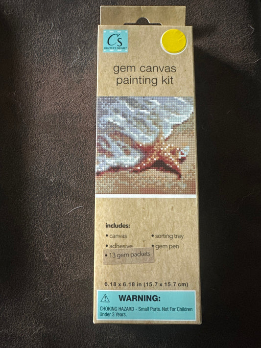 Cardboard packaging of a gem canvas painting kit of a starfish on the beach at the edge of the water on a dark textured surface