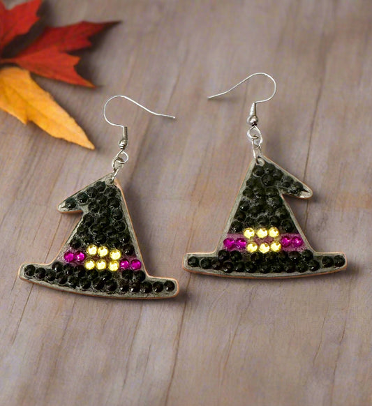 Witch hat earrings with beaded details on a wooden surface with autumn leaves.
