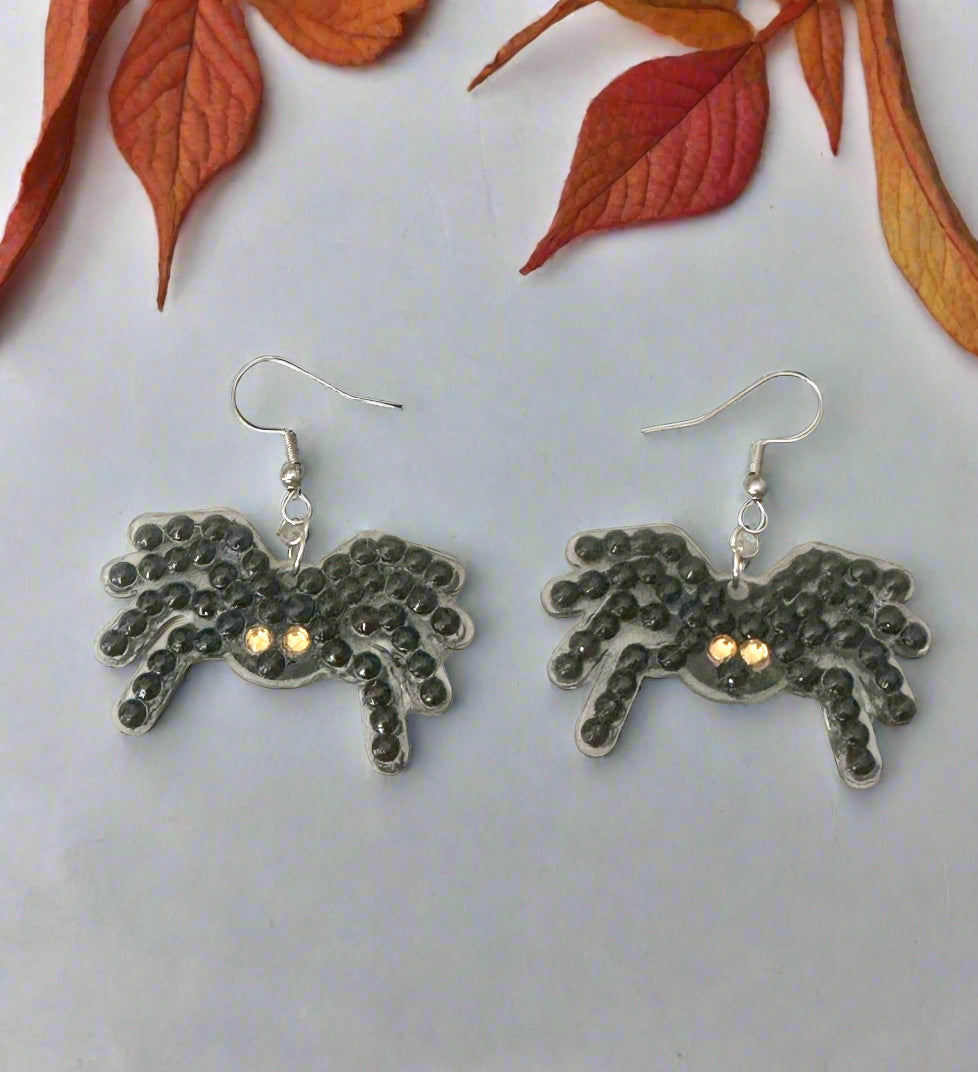 Spider earrings on a light gray background with autumn leaves.