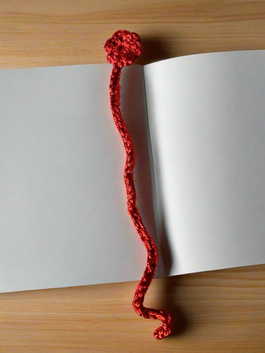 Red crocheted flower bookmark on an open book with a wooden surface underneath