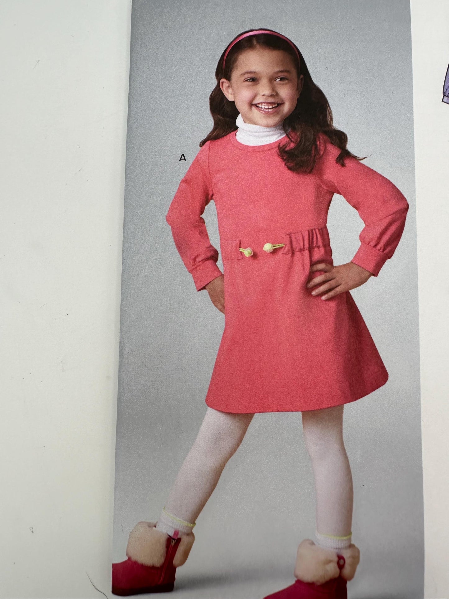 Young girl wearing a pink dress with a white collar and red shoes on a gray background