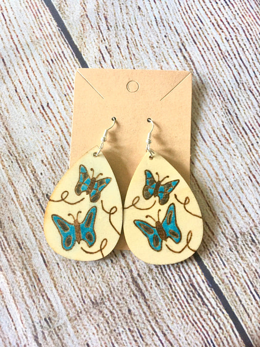 Wood burned earrings wood burned with butterflies colored blue.  Earrings have fishhooks and are teardrop shape.