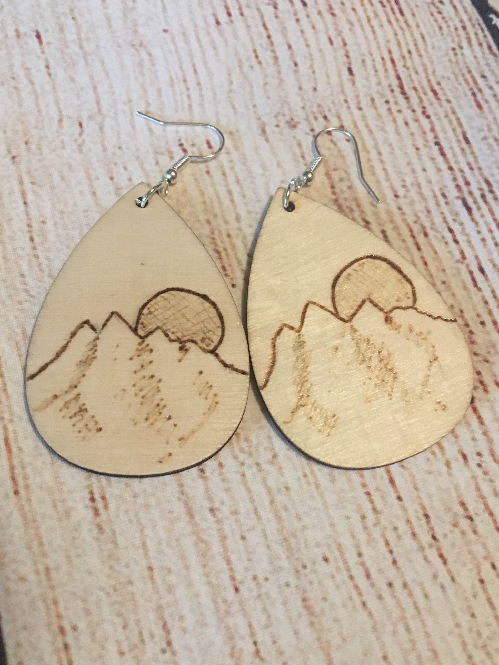 Wood burned earrings wood burned featuring a mountain and the sun or moon.  Earrings have fishhooks and are teardrop shape.