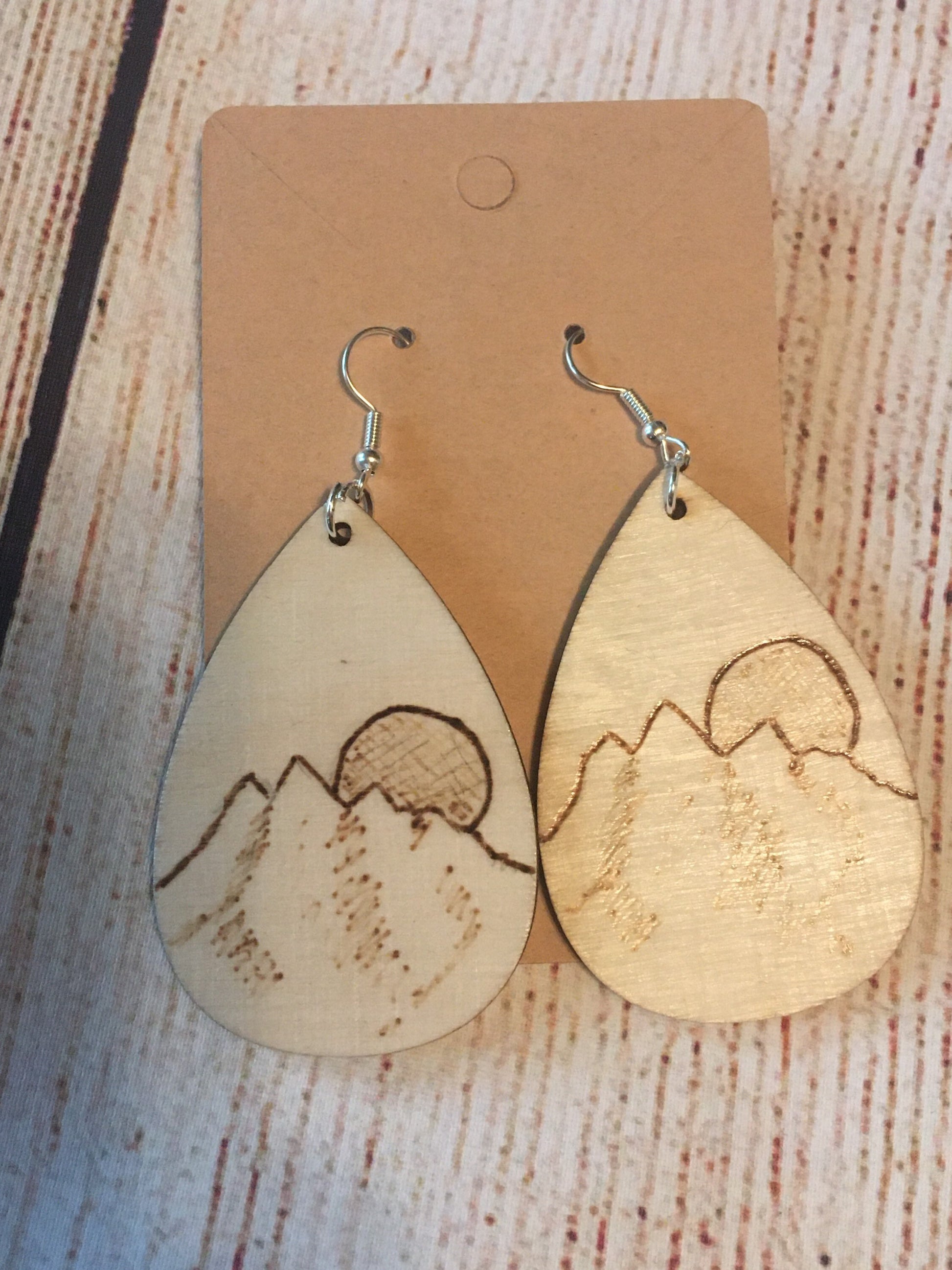 Wood burned earrings wood burned featuring a mountain and the sun or moon.  Earrings have fishhooks and are teardrop shape.